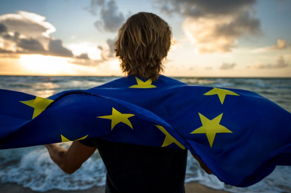En man som står på en strand och har en europaflagga runt axlarna
